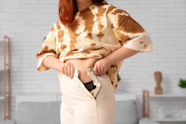 Image of woman trying to do her trousers up after pregnancy weight gain Higham Ferrers
